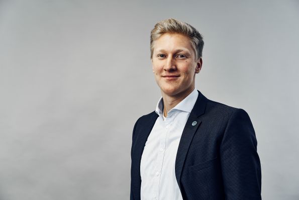 Portrait von Felix Hake, lächelnd, im Sakko vor hellem Hintergrund.