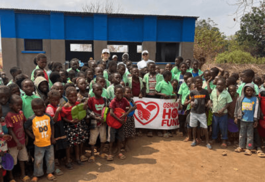 Group of children in school uniforms holding an Osmow's Hope Fund banner