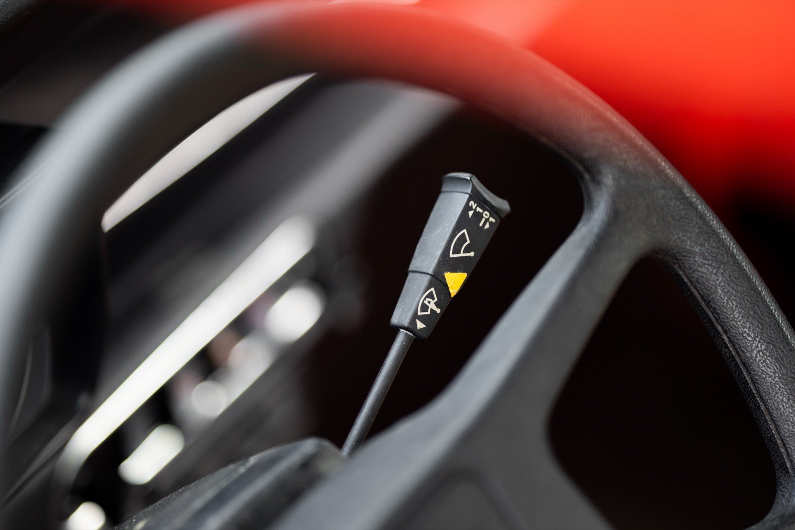 Close-up of a car steering wheel with controls, featuring a gear shift and a bright red background.