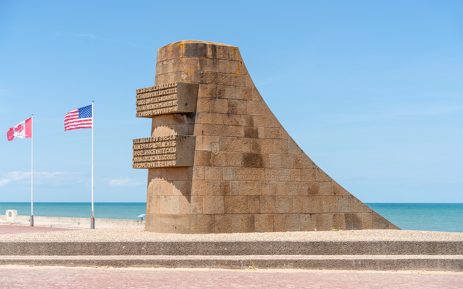 Normandy D-Day monument with Canadian and American flags by the beach.