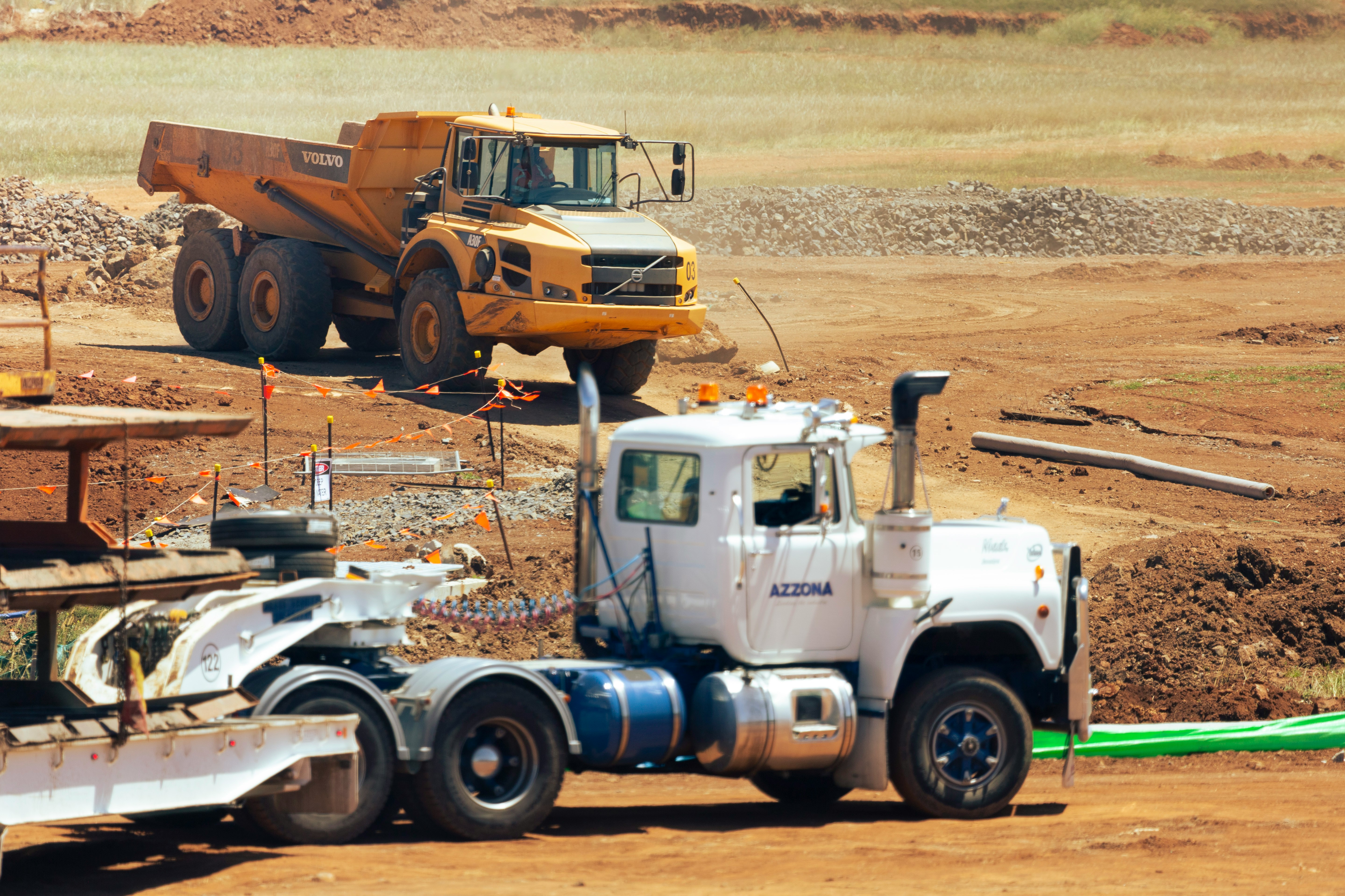 photo of two trucks at a construction site. One truck is yellow and appears to be approaching carrying concrete, the other white truck appears to be parked