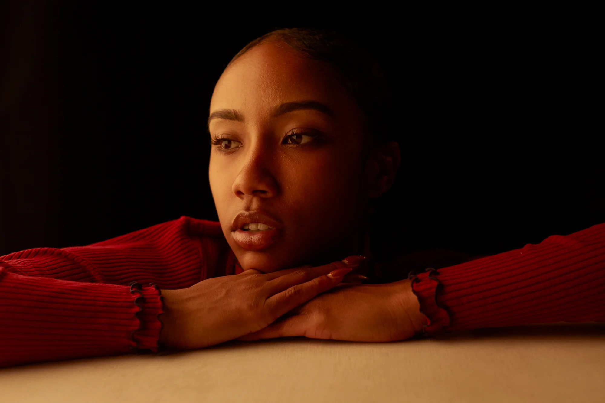 A photograph of a woman in a red long sleeve stylish shirt with directional lighting by Acquille Dunkley.