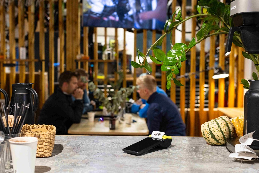 a restaurant counter with a Teya card machine over it, and a table of 4 people in front of the counter
