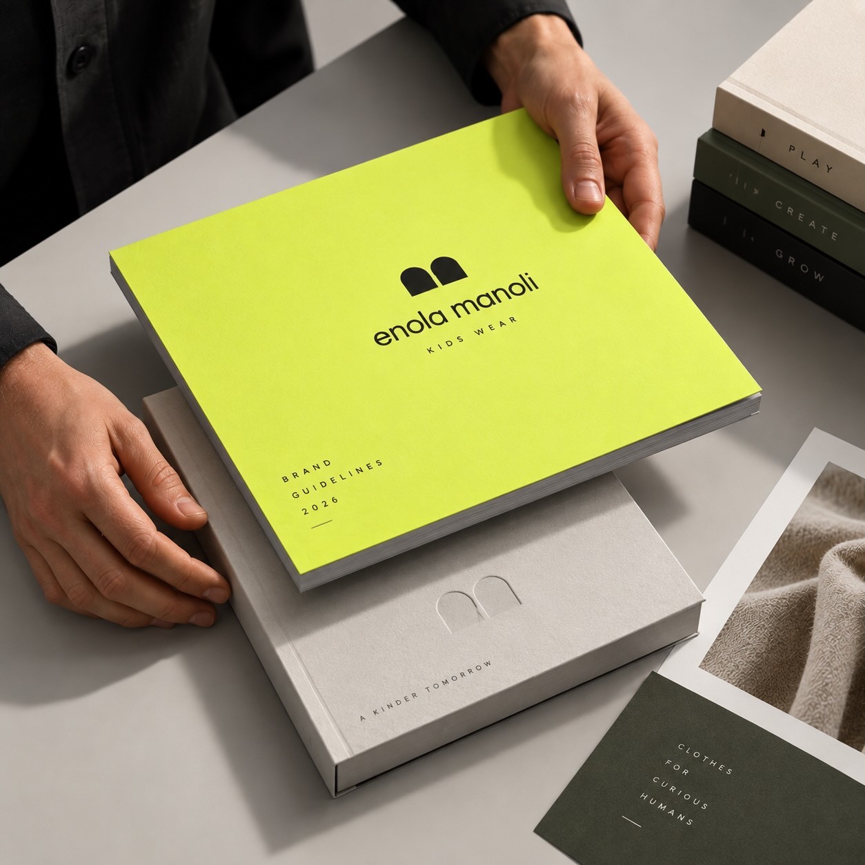Hands holding the neon yellow Enola Manoli brand guidelines book above its box