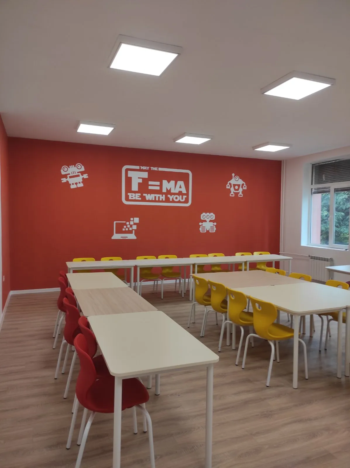 Classroom with yellow school chairs, white tables, and red wall graphics