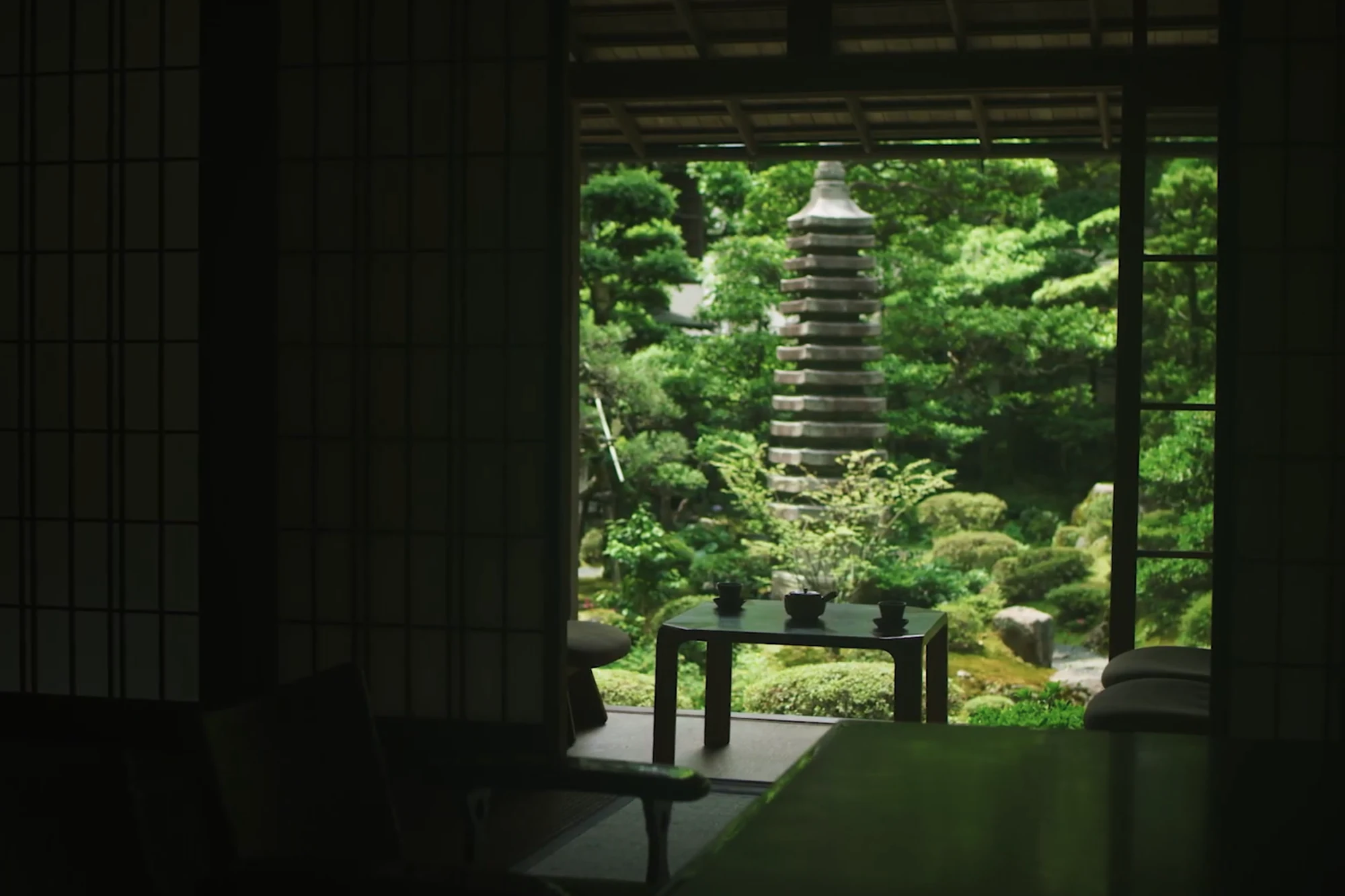 A tatami guest room in a Kinosaki inn with shoji opened onto a garden and a low table set for tea.