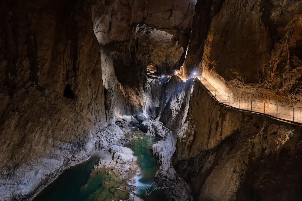 A river flowing through a huge cave canyon with a lit up path leading along the walls in Škocjan caves, Slovenia.