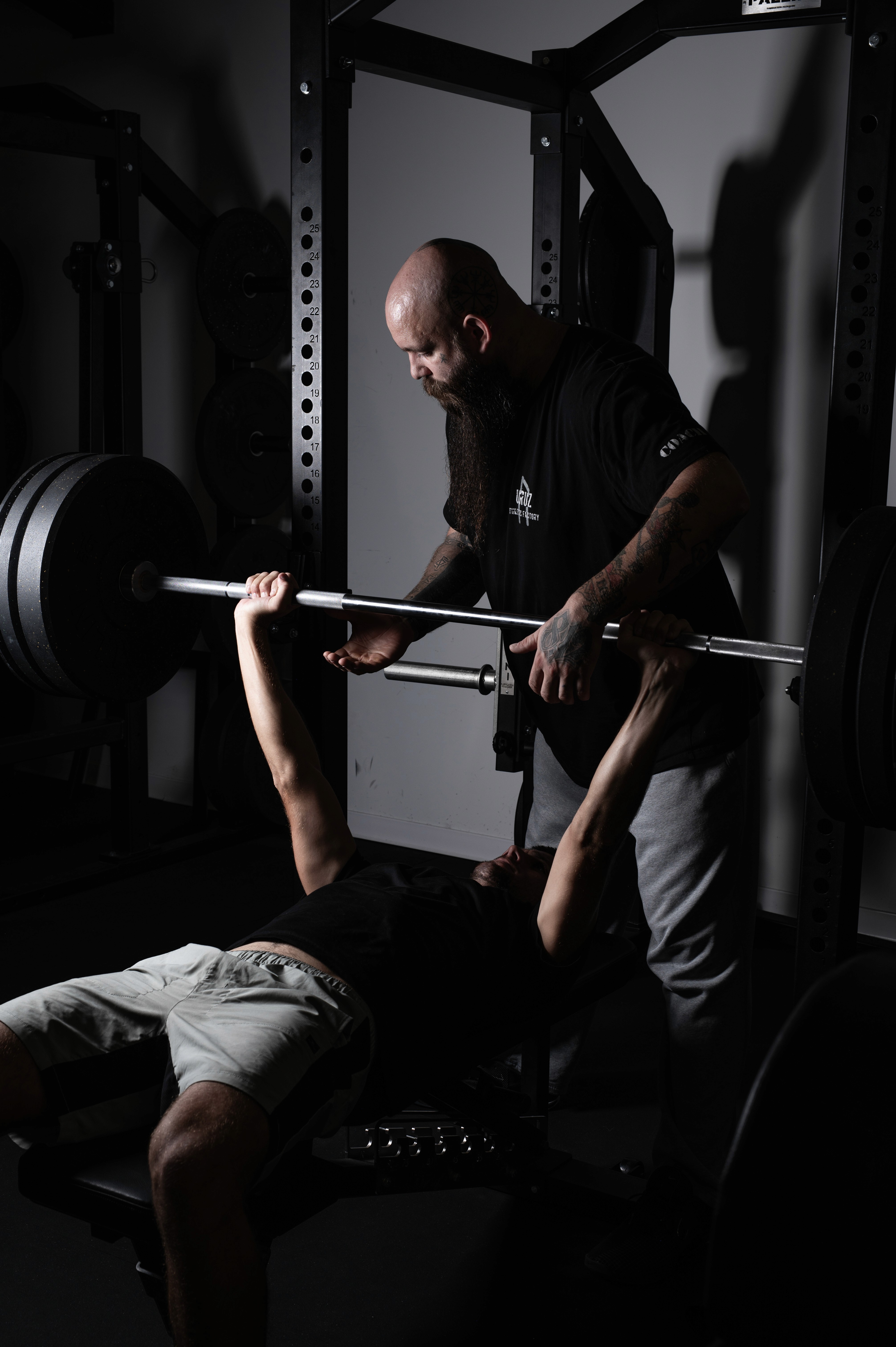 Two individuals are working out in a gym, focusing on dumbbells and strength training equipment.