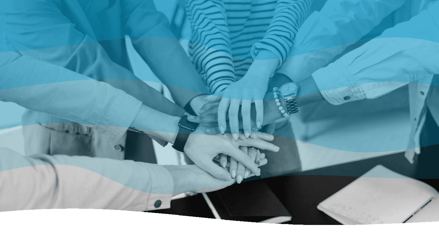 A diverse group of people place their hands together in a unity gesture over a table with notebooks, creating a sense of teamwork and collaboration.