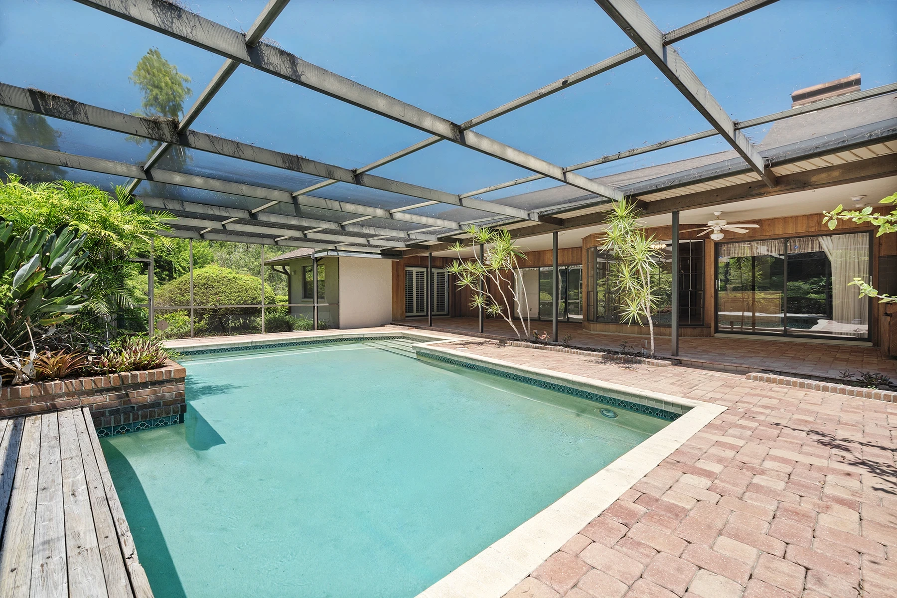 Screen-enclosed pool with brick paver deck and tropical landscaping at a Florida home