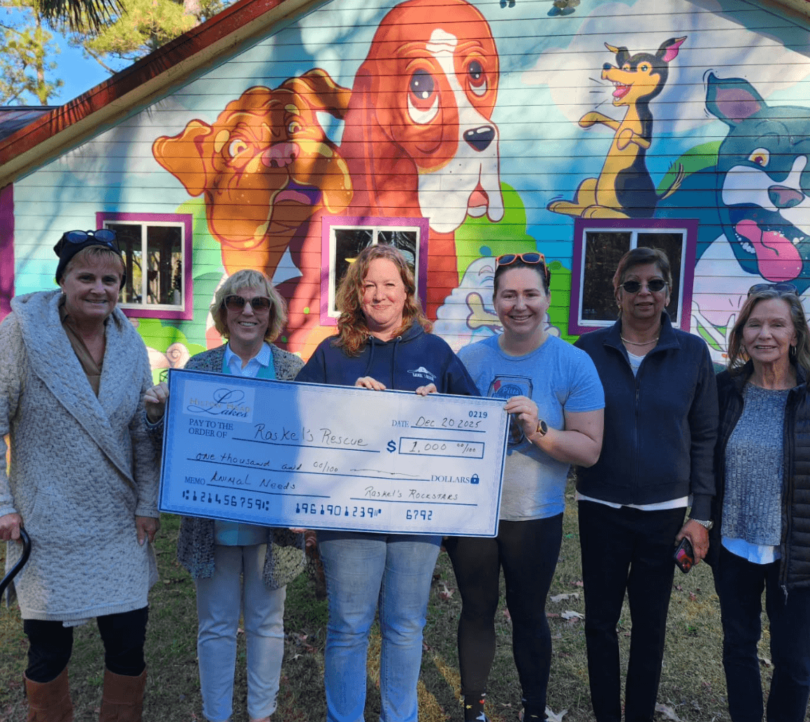 A group of six people stands in front of a colorful mural, holding a large check.