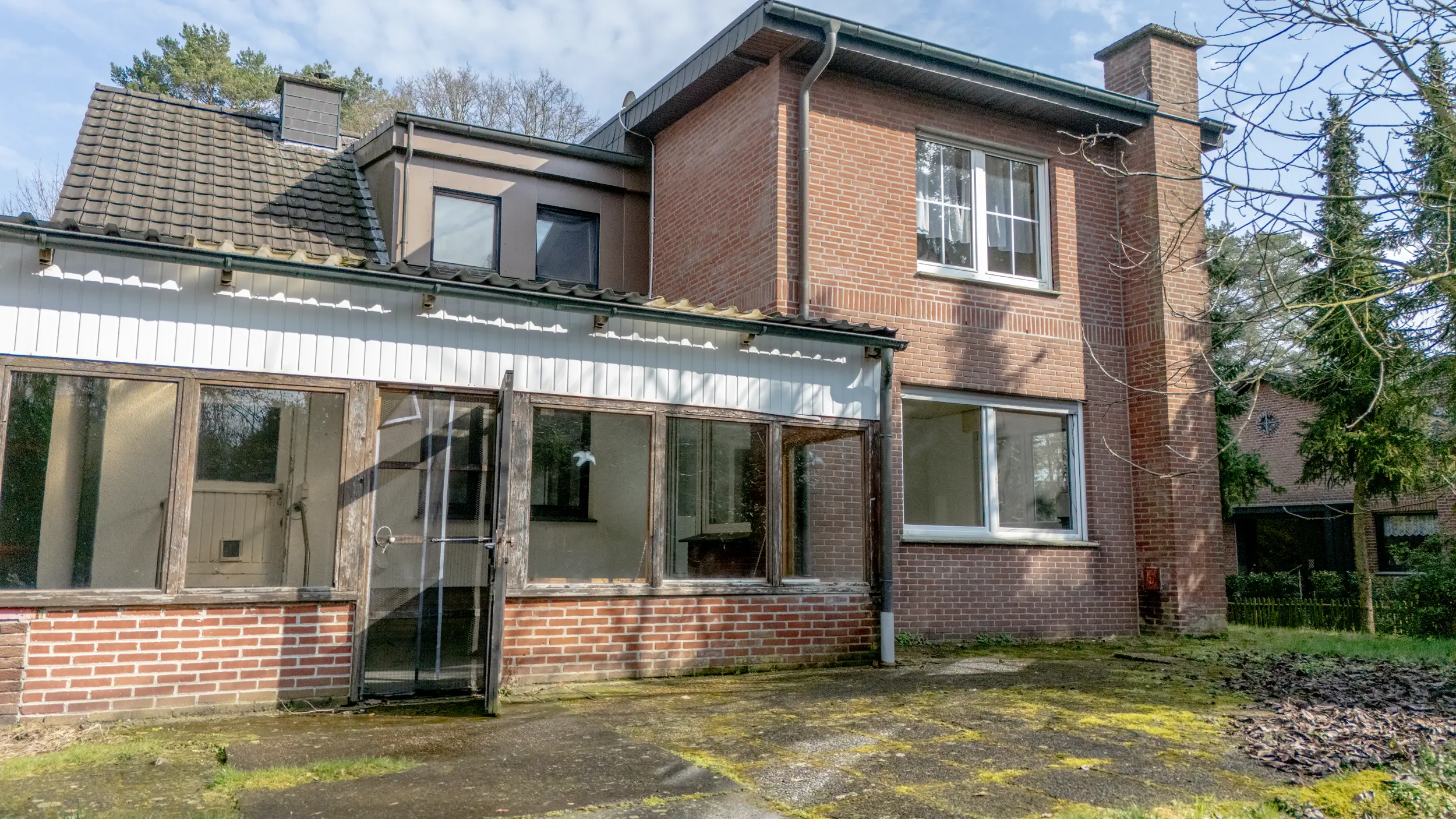 Rückansicht des Hauses mit verglastem Anbau, Klinkerfassade und befestigter Terrasse auf dem Grundstück in Gronau-Epe.