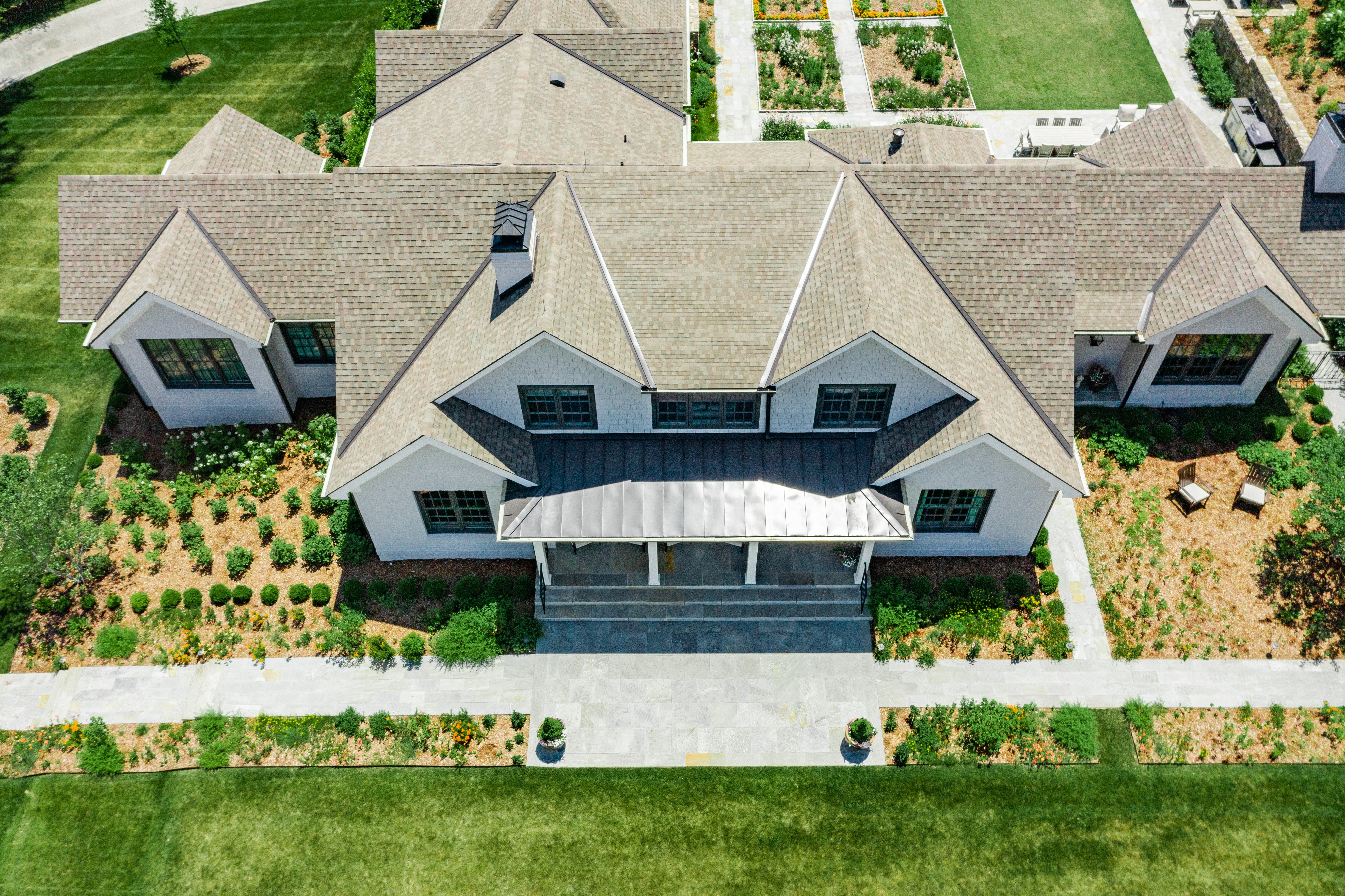 Aerial view of a spacious house with a gray roof, surrounded by well-maintained lawns and gardens.