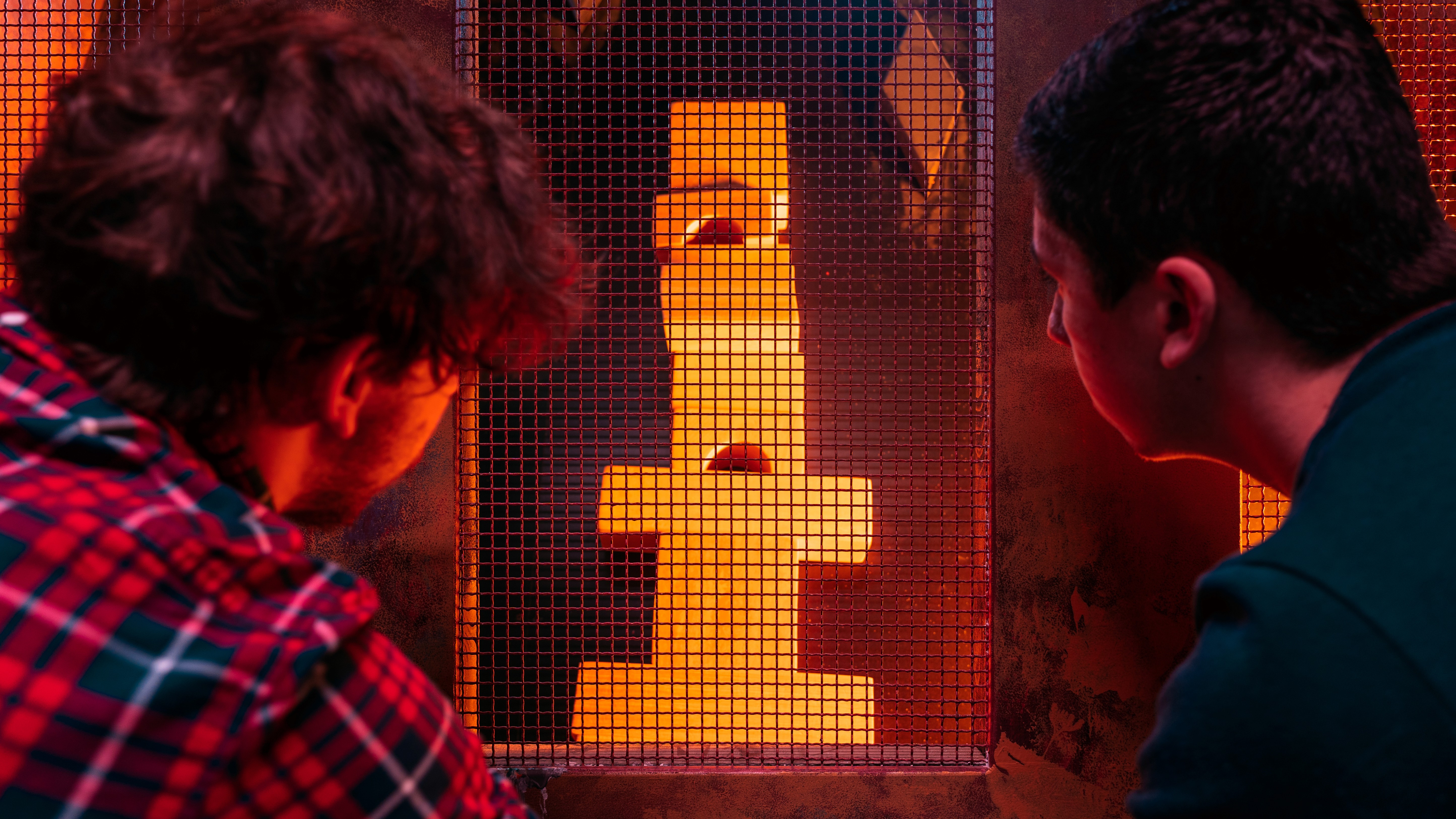 A young person with curly hair smiles at the camera while sitting in front of a laptop against a dark background.