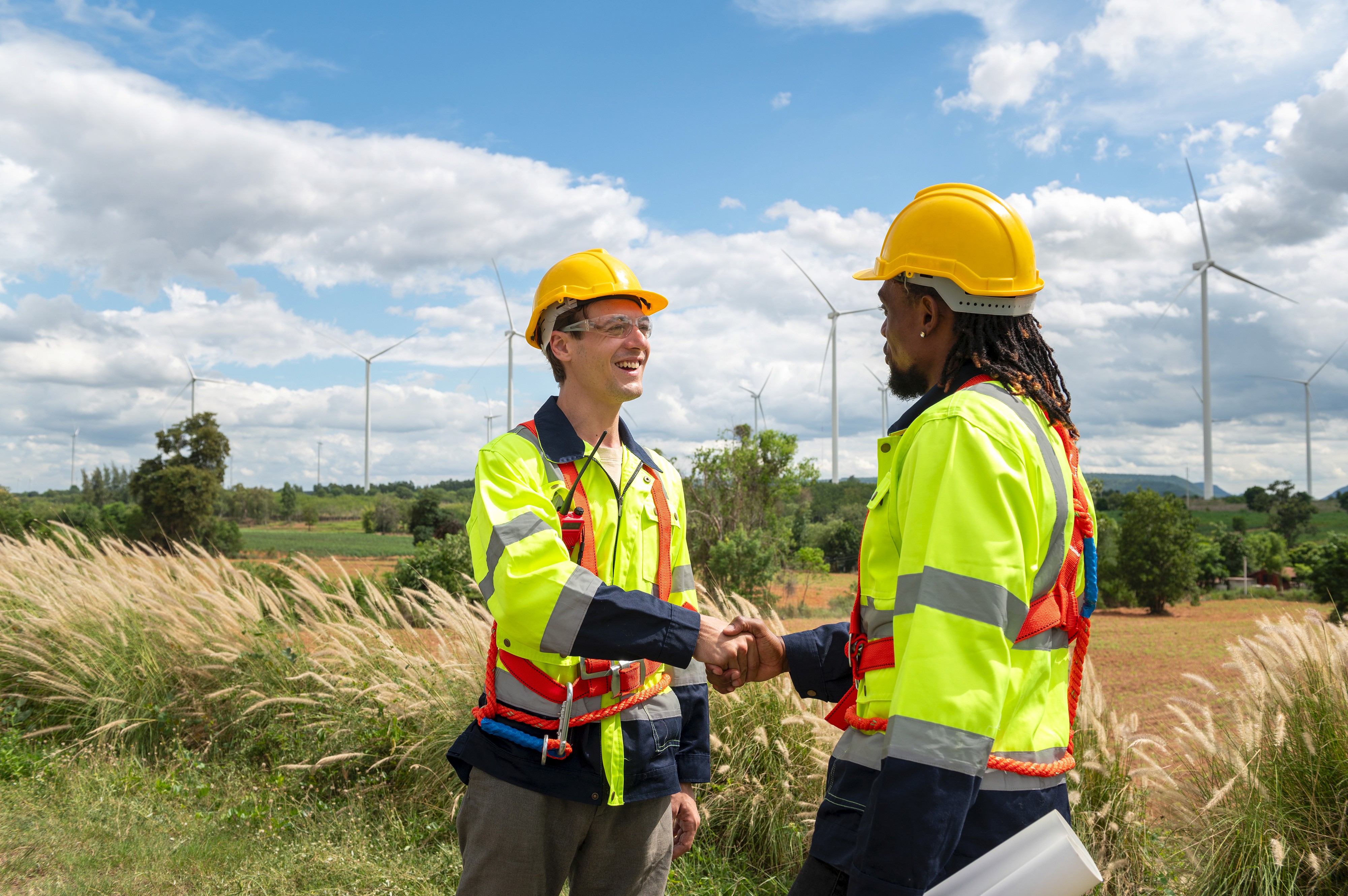 Two engineers shaking hands in a summer field against blue sky and clouds.