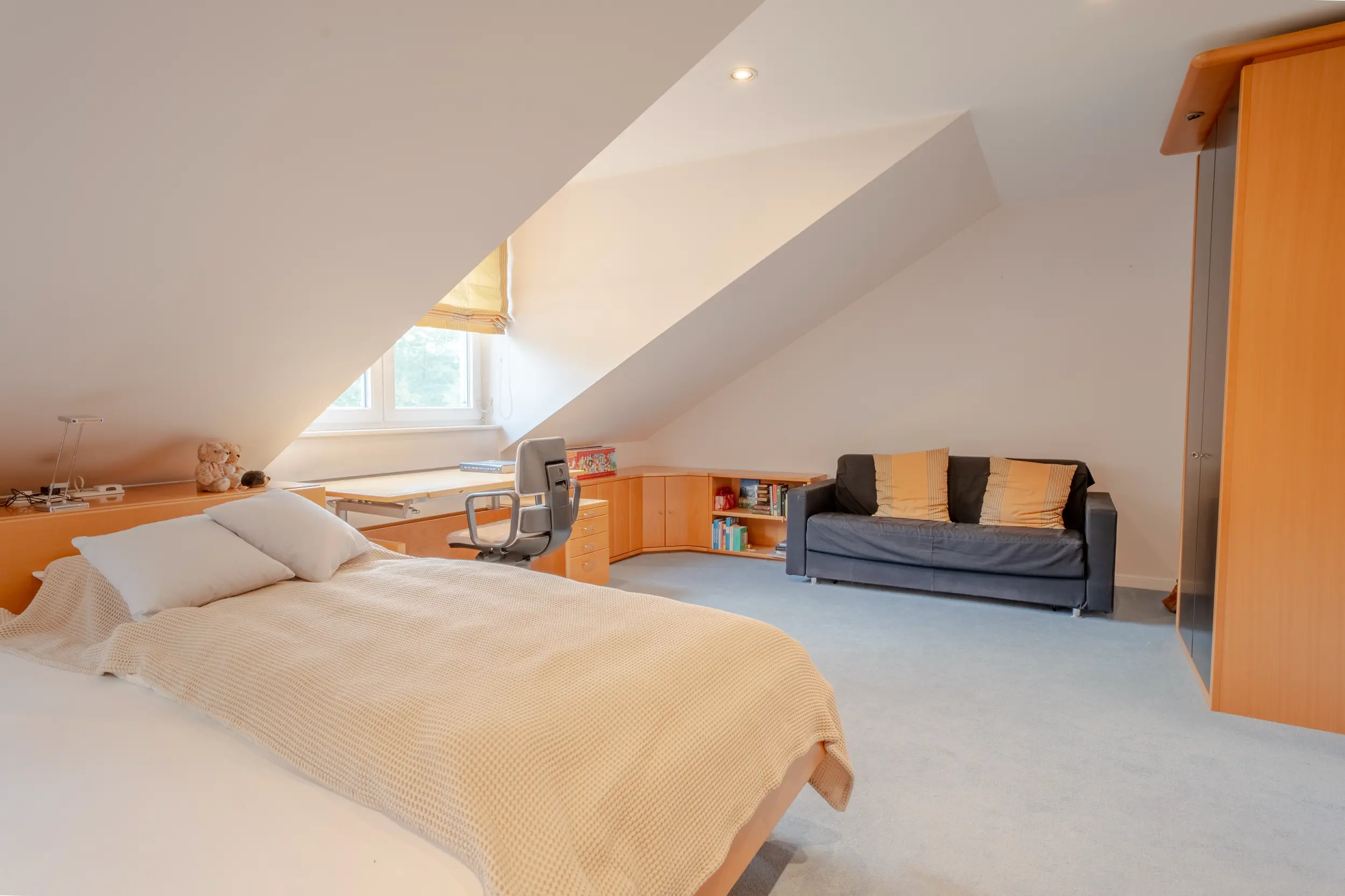 Modernes Dachgeschoss-Schlafzimmer der Villa Gronau mit Home-Office, Sofa und Holzmöbeln unter Dachschräge – Westfalen Wohnen