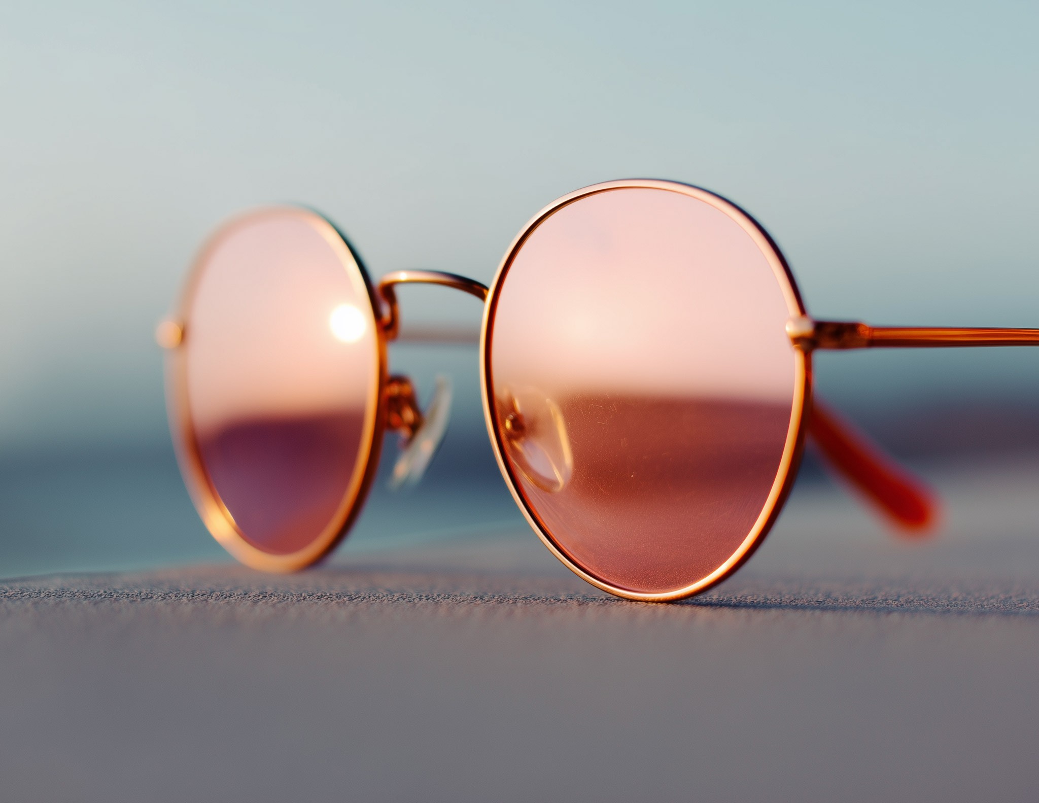 Rose gold round sunglasses resting on sandy beach