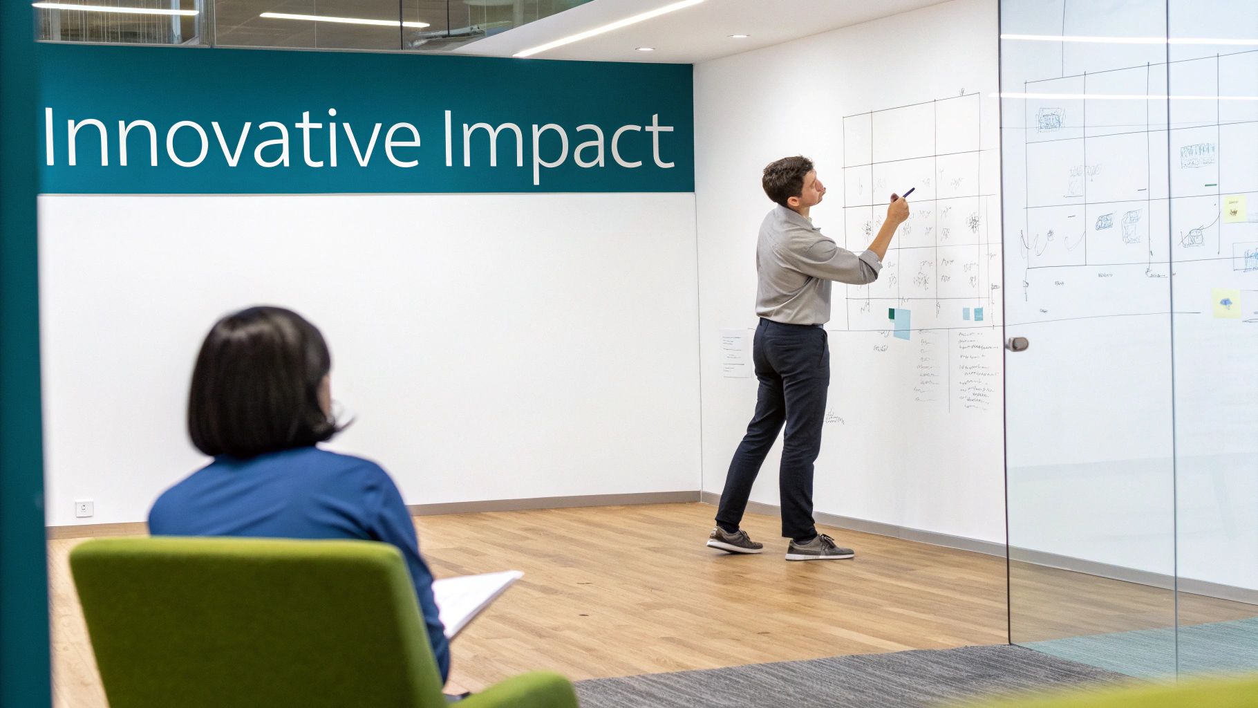 A man brainstorms on a large whiteboard in a modern office, while a woman observes.
