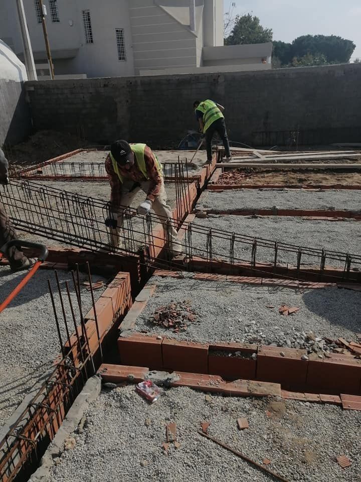 A modern hallway features vibrant teal and orange geometric and leaf patterns, with glossy tiled floors, a large rectangular light fixture, and a small shelf holding a potted plant, all leading to a large, frosted window at the end.