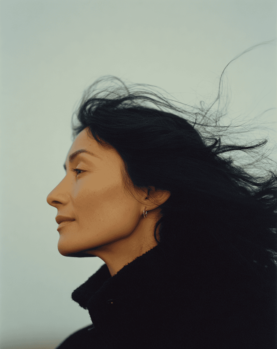 Side profile portrait of a woman in a dark coat with wind-blown hair.