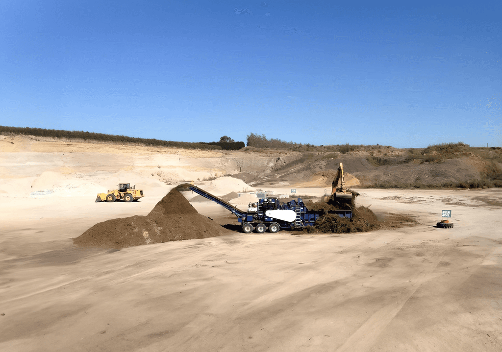 Green waste being mulched in a sand quarry with a digger and a loader