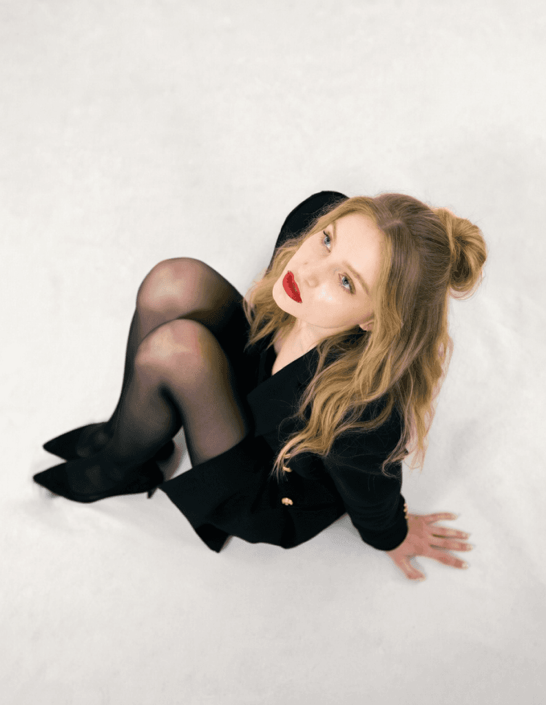Woman in a black outfit sitting on the floor looking up in a studio
