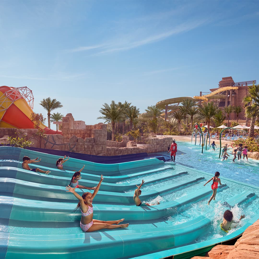 Children enjoying waterslides at Atlantis Aquaventure Waterpark in Dubai, supervised by a lifeguard, part of top family activities in Dubai.