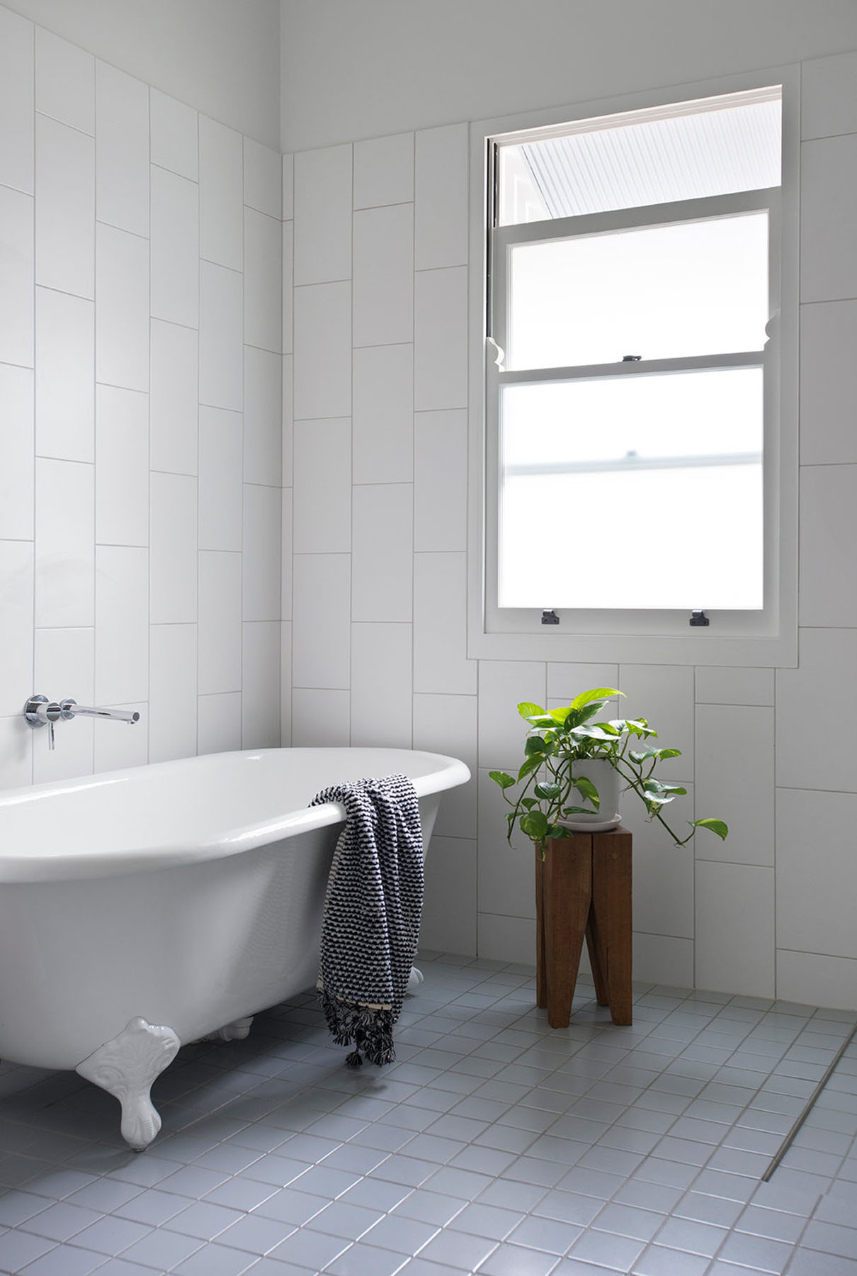Compact bathroom with freestanding tub, tiled walls, and softened daylight through frosted glazing