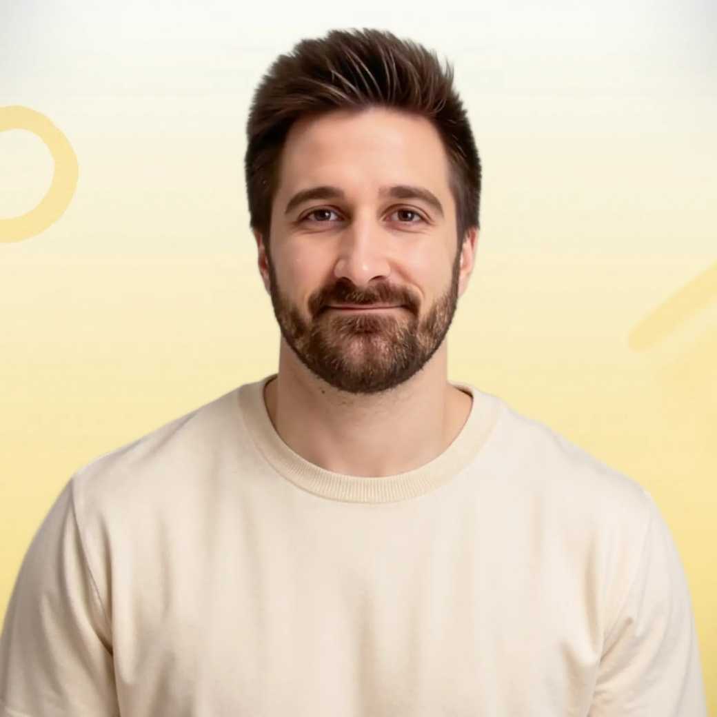 Smiling man with light brown hair and stubble, wearing a khaki shirt in natural light