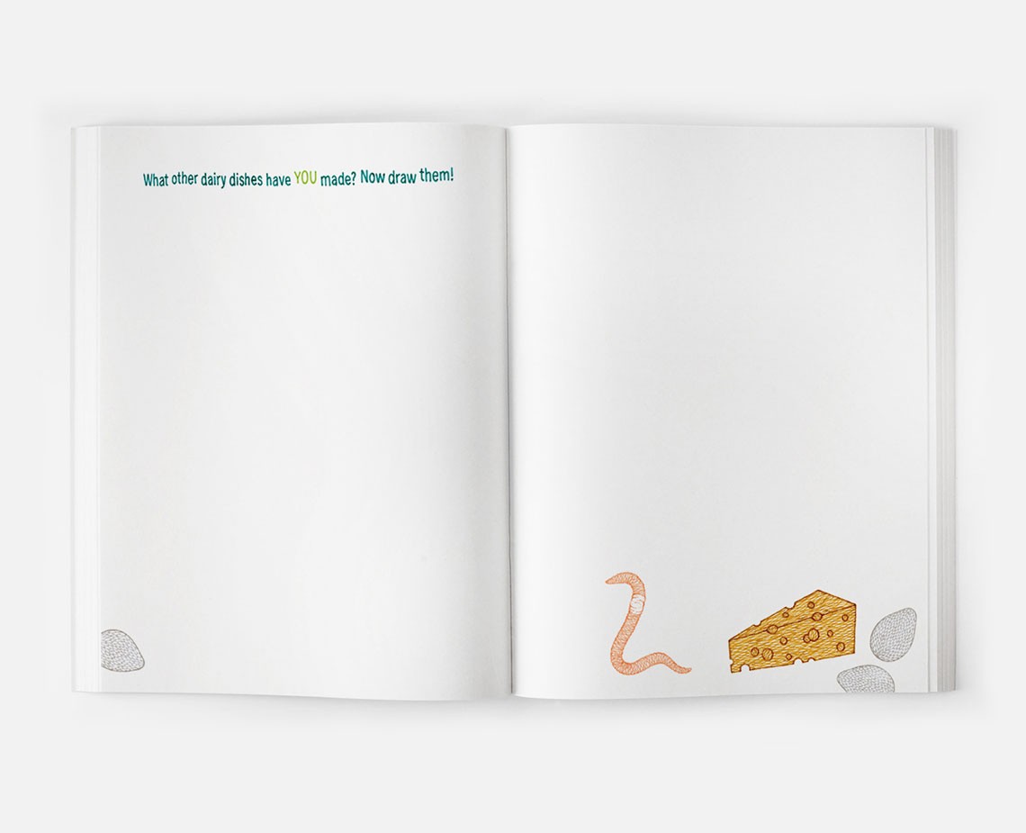 An open book displays a blank page on the left and a page with illustrations on the right. The left page contains the text "What other dairy dishes have YOU made? Now draw them!" in blue and yellow text. The right page features a drawing of a worm next to a wedge of cheese, with gray rocks at the bottom.
