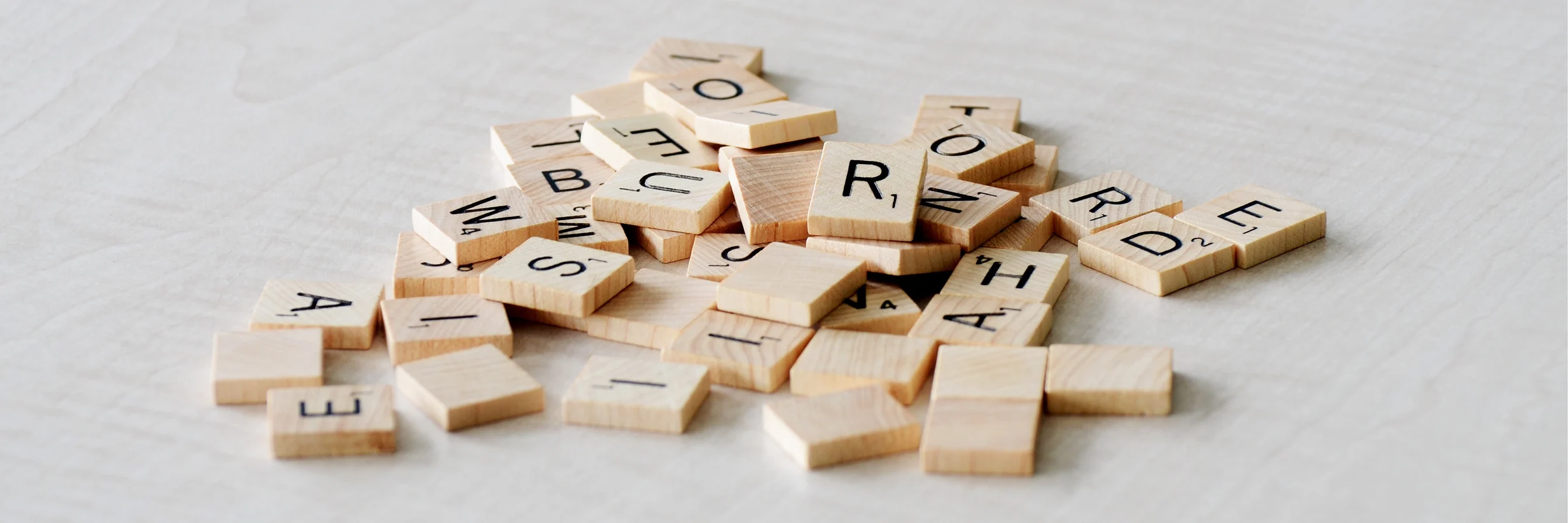 A close-up of scattered wooden Scrabble tiles forming random letters.