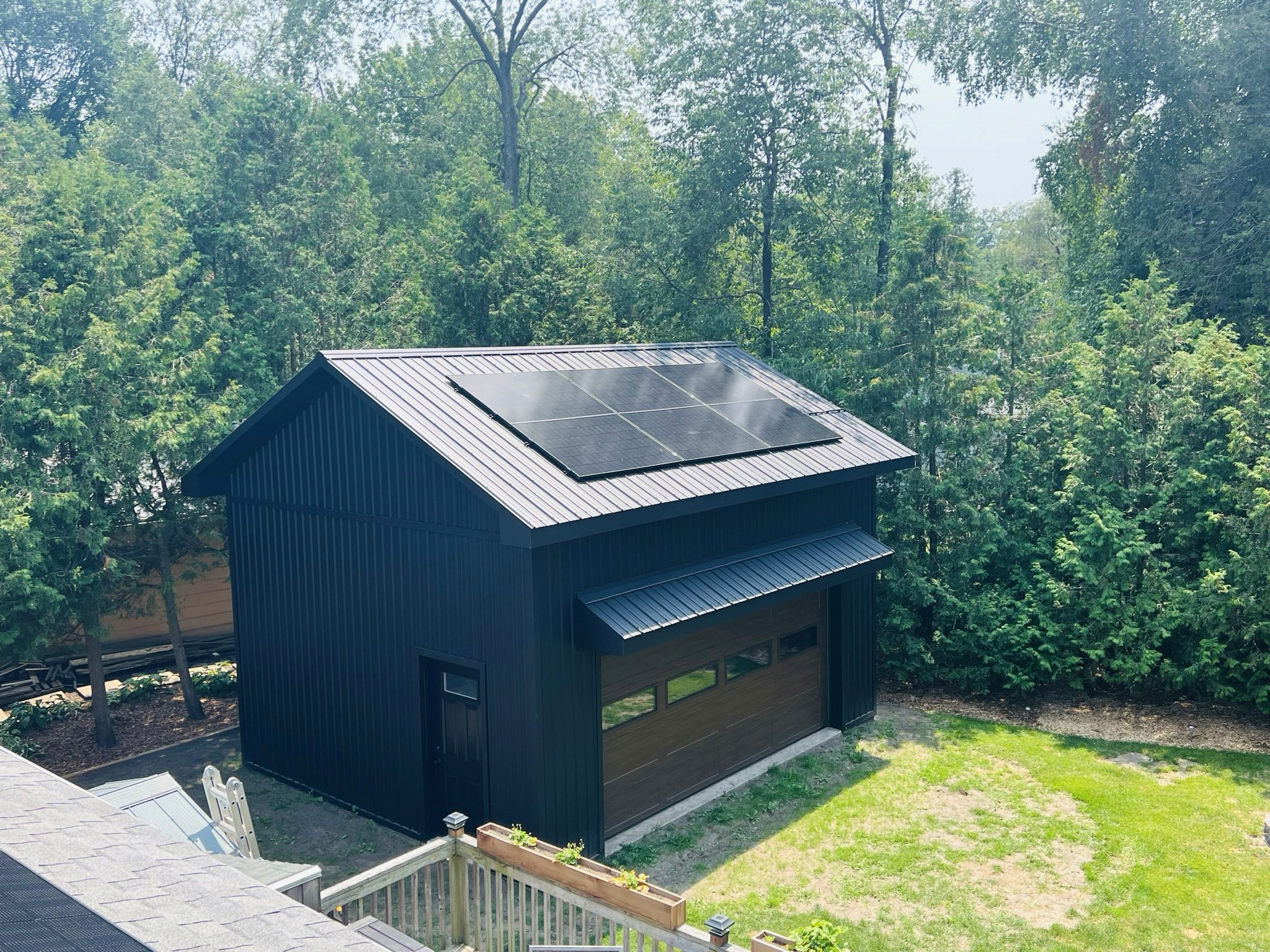 A detached garage with Solar panels on the roof, surrounded by greenery located in Hamilton Ontario.  