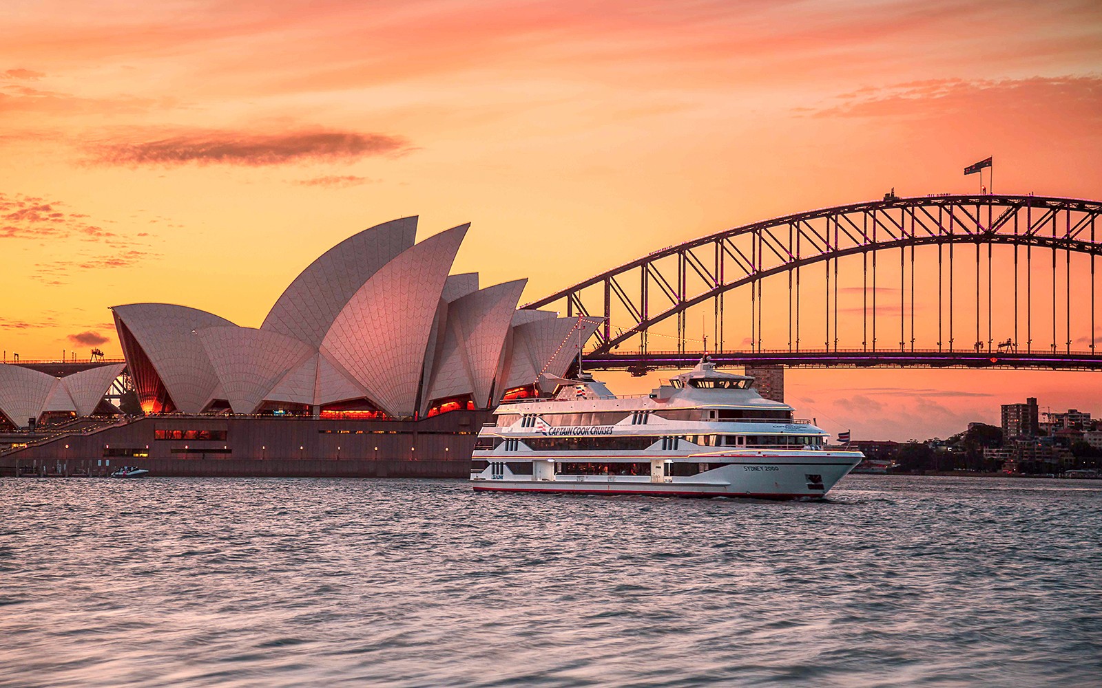 Captain Cook Cruise bij zonsondergang nabij het Sydney Opera House en de Harbour Bridge.