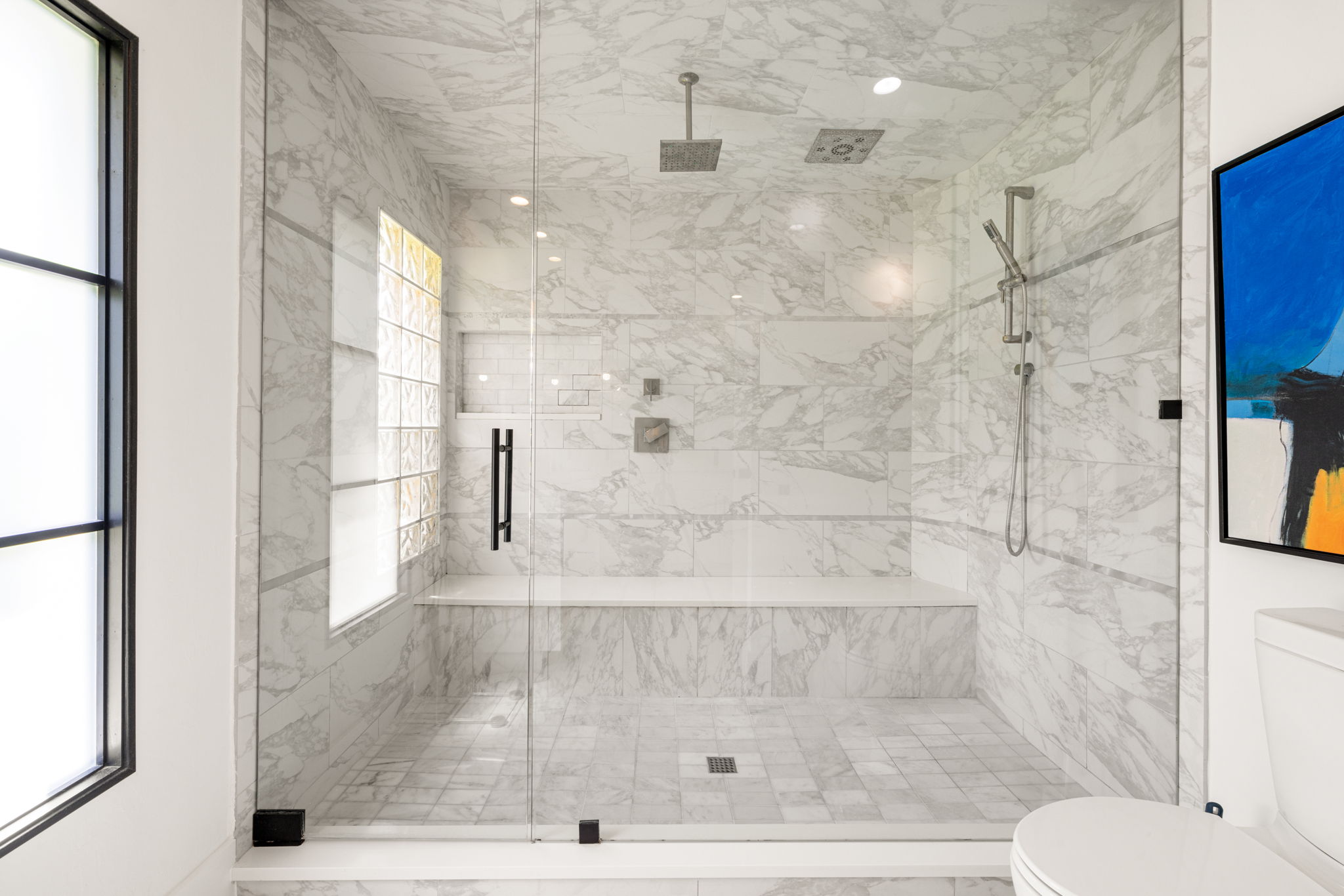 a modern white shower with white tile and large windows allowing natural light to shine through