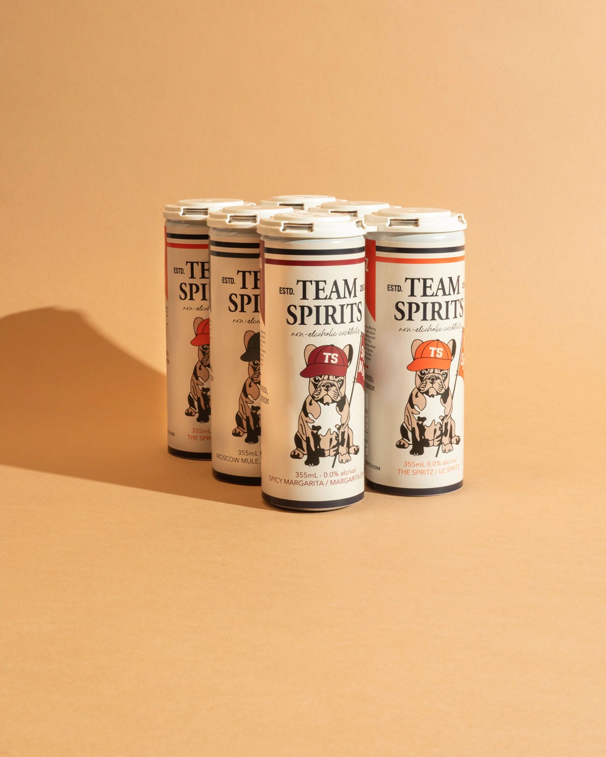 Studio product shot of ‘Team Spirits’ canned beverages at Node Studio, styled against a warm beige background to emphasize the vibrant branding and crisp packaging design