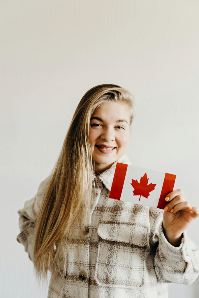 A smiling newcomer holding a small Canadian flag, representing a successful Express Entry applicant who navigated the true hidden costs of Canadian Permanent Residency (PR) in 2026 without overpaying for immigration consultant fees.