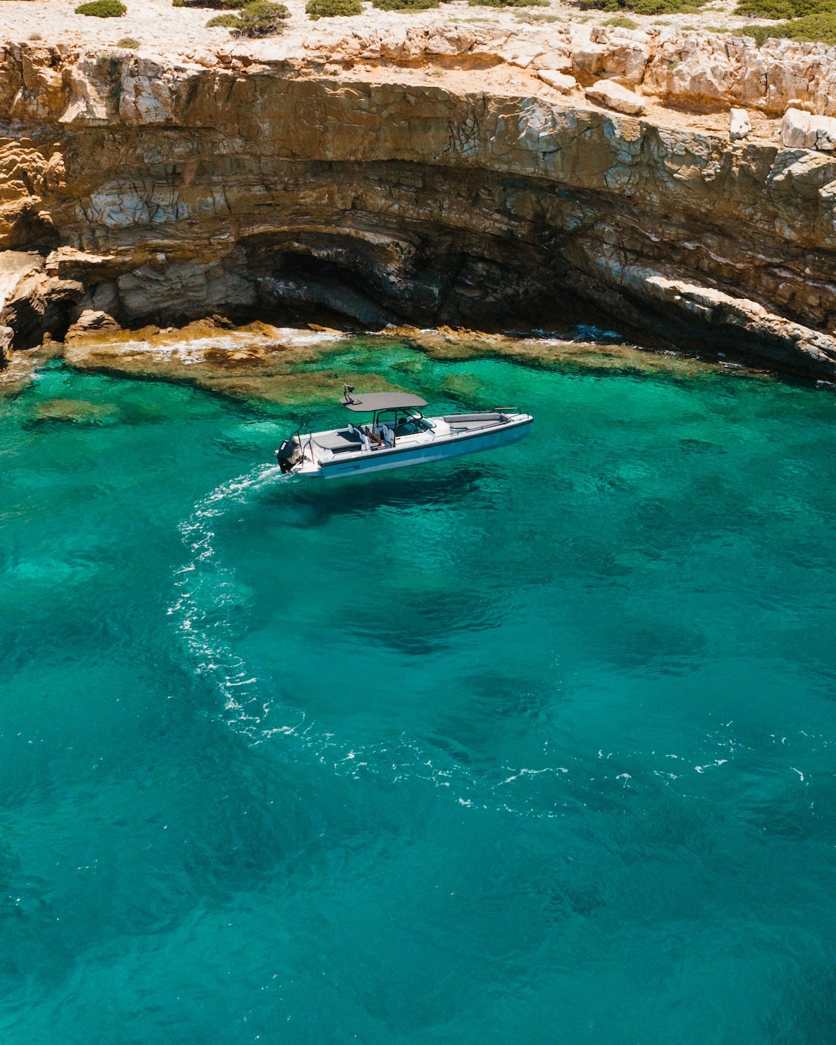 White Axopar 37 yacht named "Anima" cruising through turquoise waters surrounded by dramatic limestone cliffs in the Cyclades.