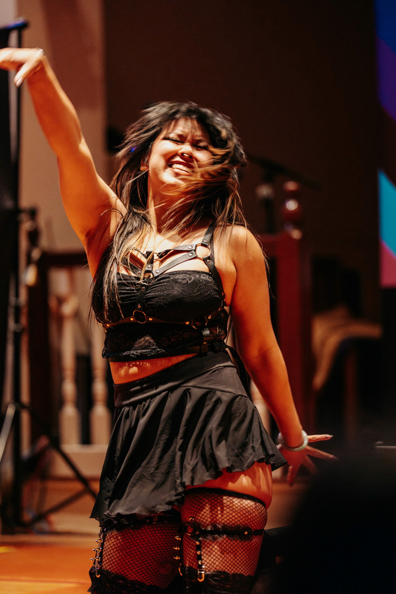 Performer smiling mid-dance during Queer Open Mic hosted by be; community in Bridgewater, Massachusetts