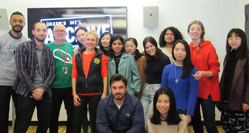 A photo of a group of people standing in front of a wall mounted tv screen.