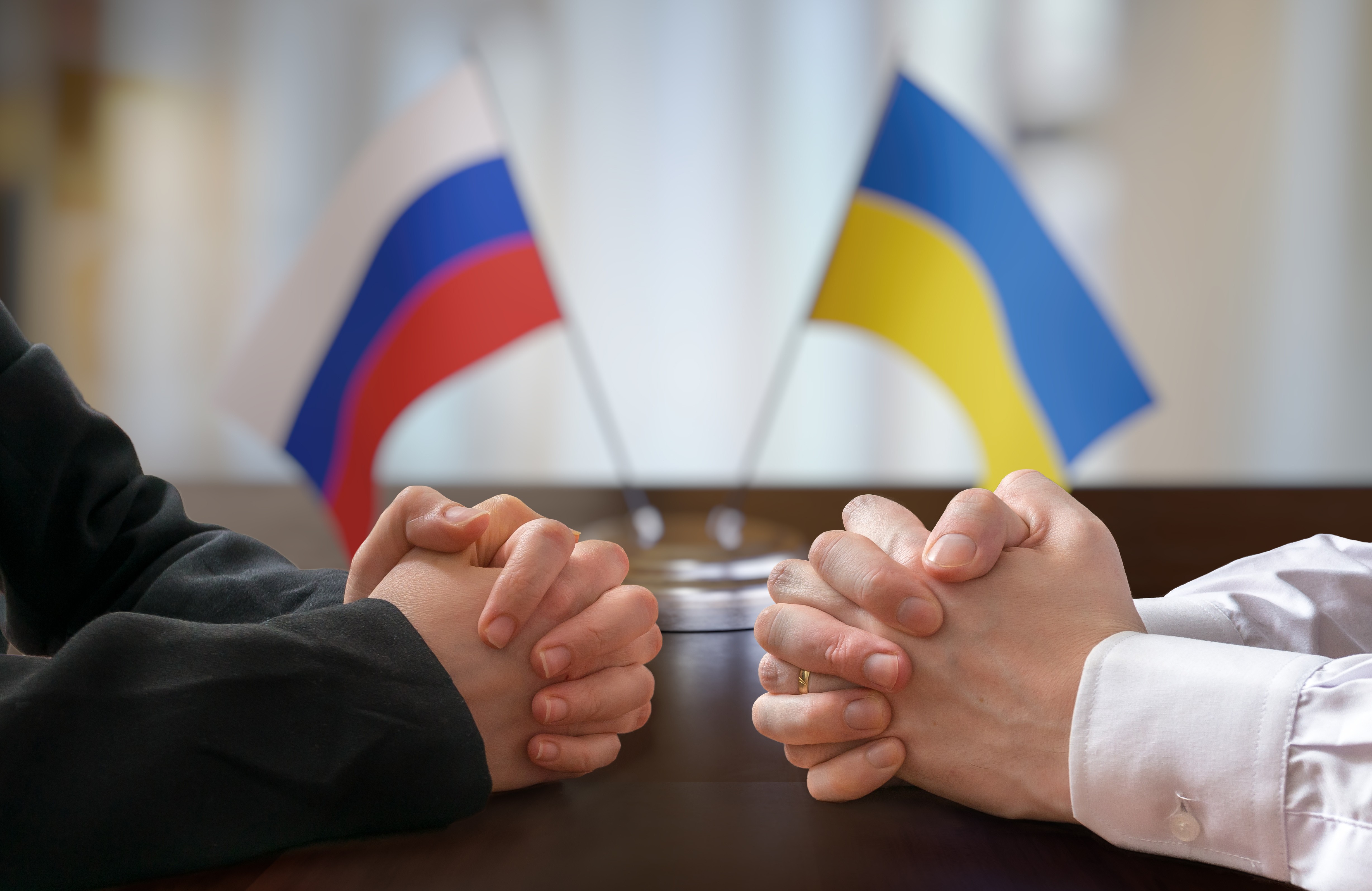 Two people sat facing one another at a table, with the Russian and Ukrainian flags in the background.