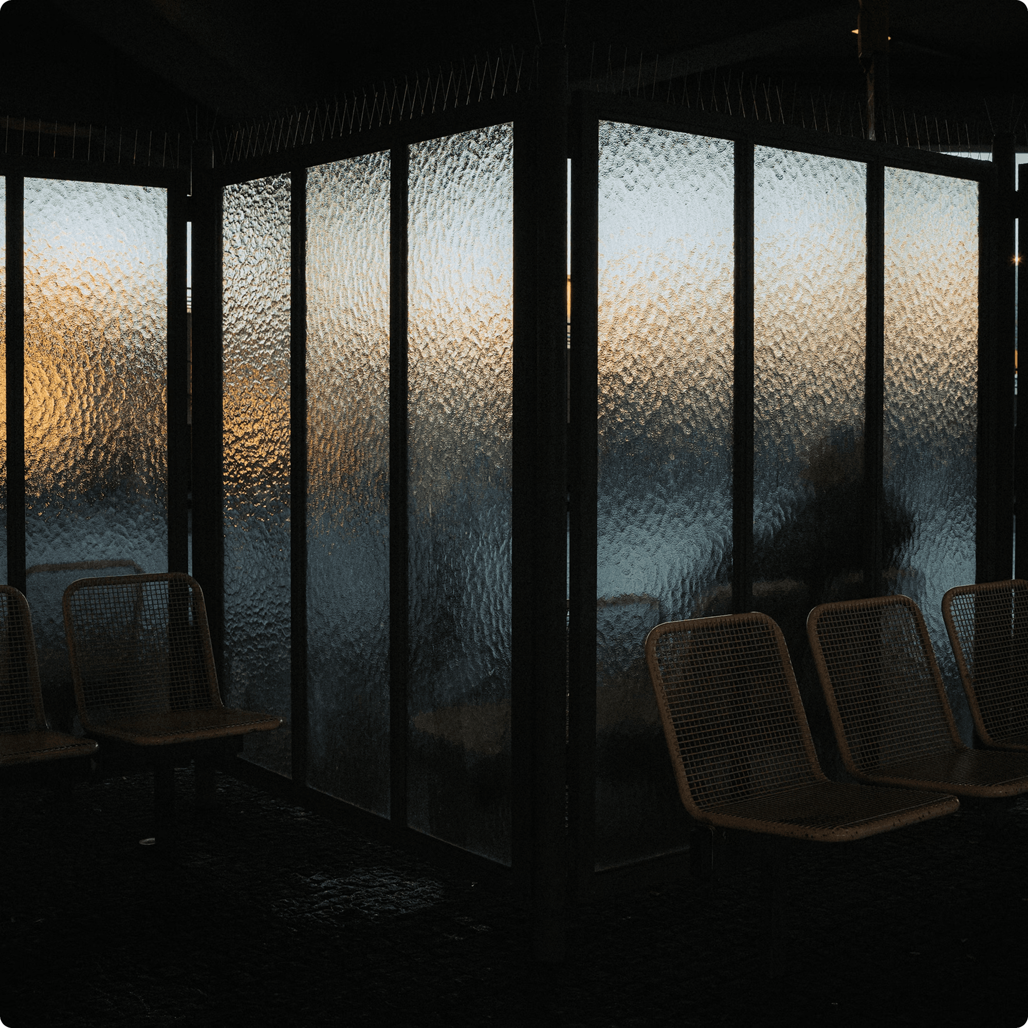 Empty mesh seats behind frosted glass panels with warm sunset light reflecting through