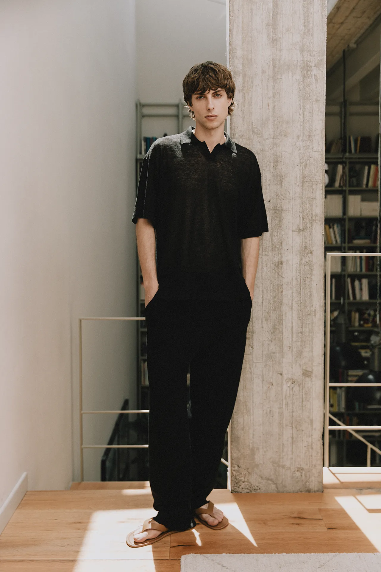 Annapurna SS26 collection men's black sheer fine-knit polo shirt paired with relaxed black trousers.