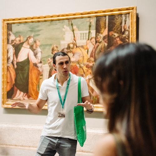 מדריך טיולים מדבר בהתלהבות עם מבקר מול תמונה גדולה ממוסגרת בתוך גלריה לאומנות.