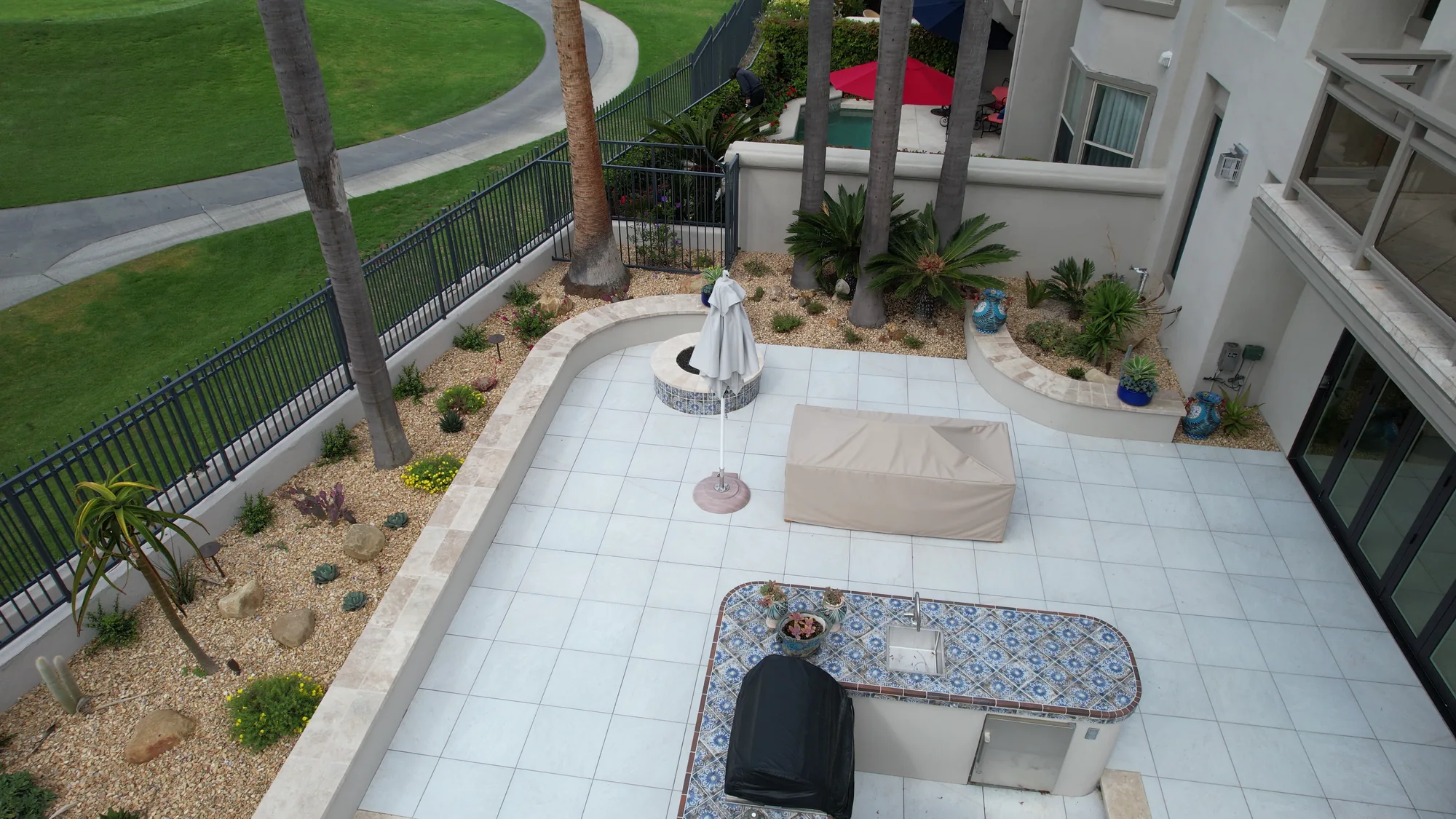 Palms and planted borders follow the curved edge of a paved terrace beside the home.
