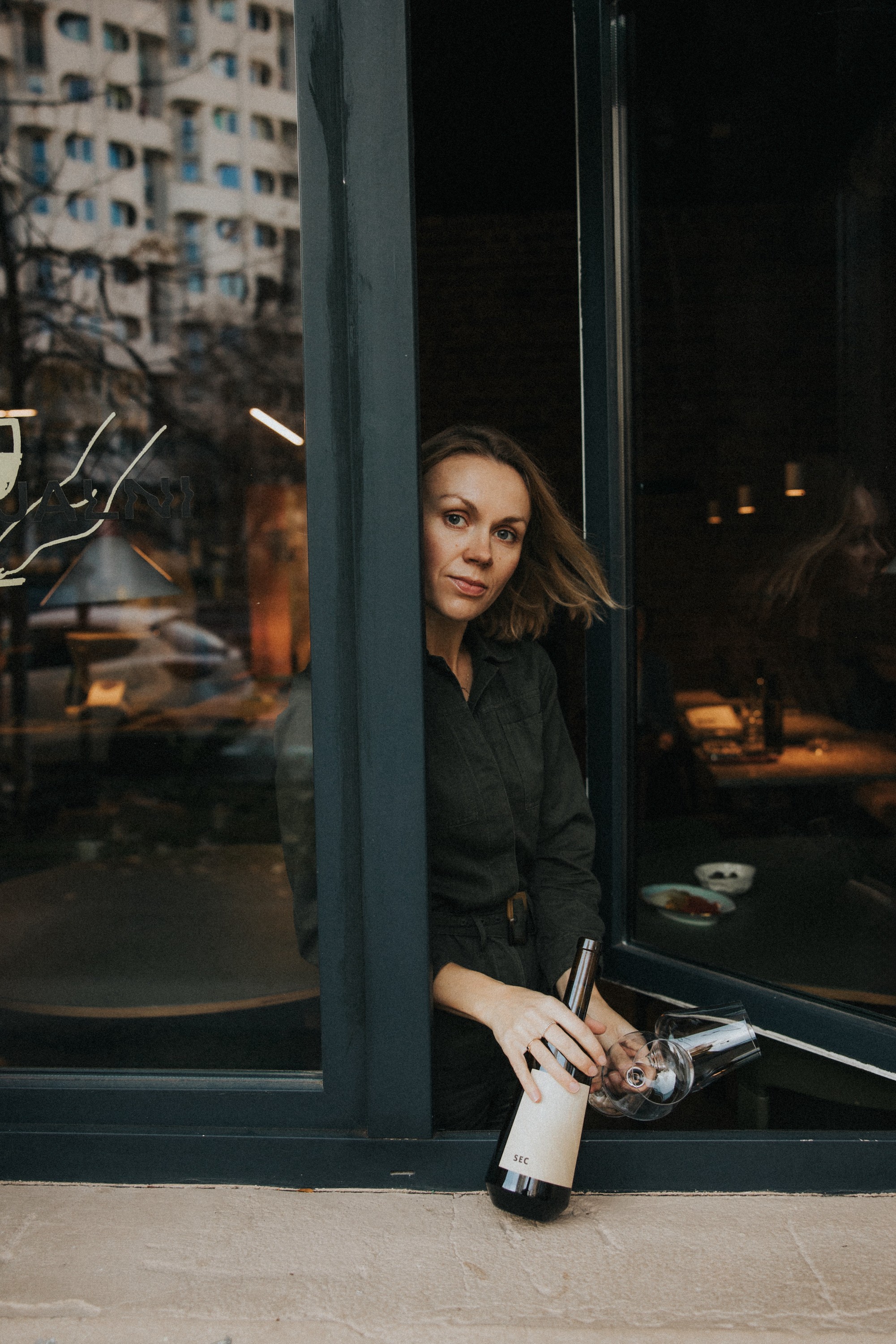 A person sits by a window, gazing thoughtfully outside, with soft lighting and city scenery in the background.