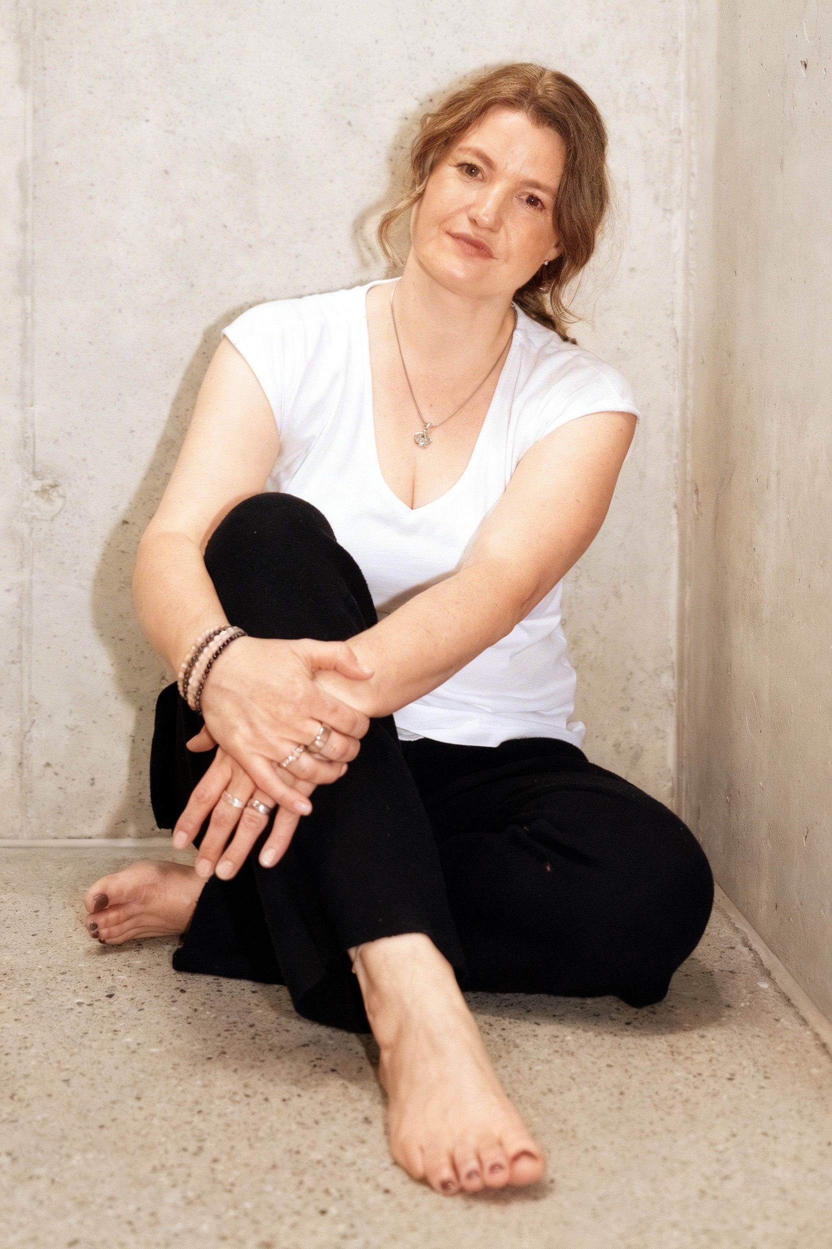 Woman standing indoors with folded arms, smiling confidently surrounded by green plants.