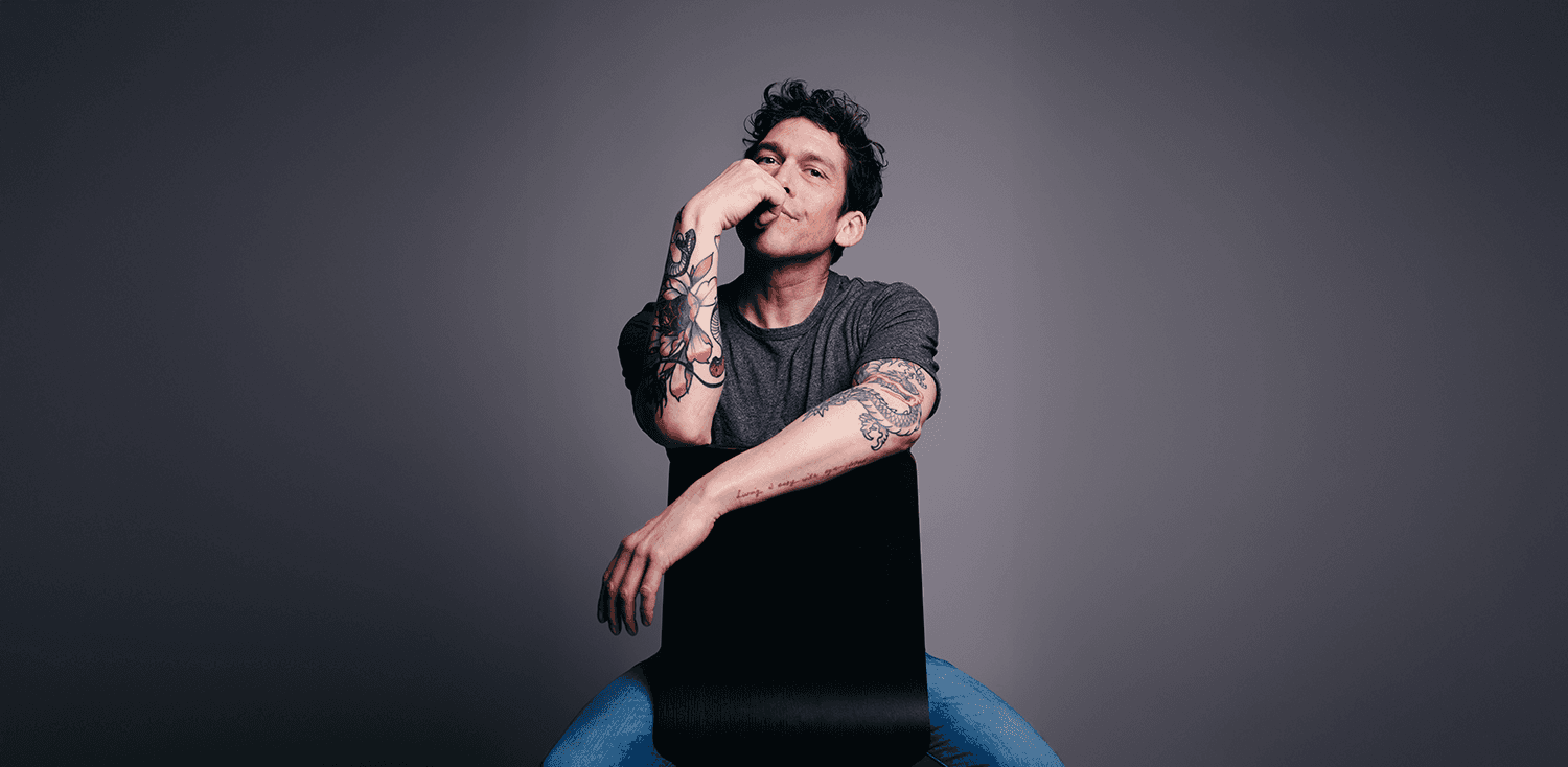 About Me hero section featuring a portrait photograph of Marco Ramos, seated and facing the camera, showing visible arm tattoos. The background is dark gray, with large white text reading 'About me' and navigation links at the top.