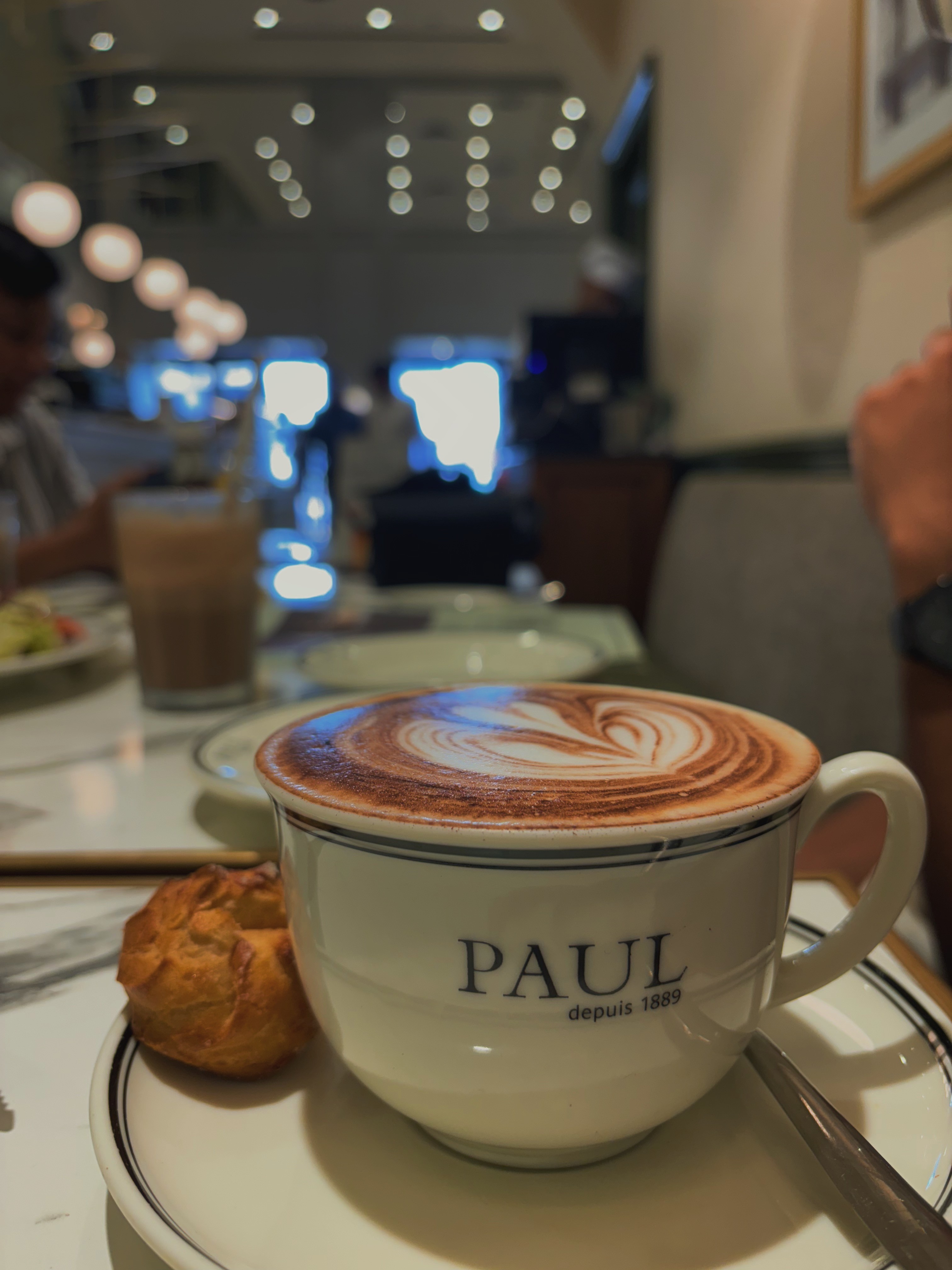 Una persona con una camiseta negra y pantalones de color claro está de pie en la cima rocosa de una montaña al atardecer, sosteniendo una cámara frente a su cara para tomar una foto. Un mar de nubes se extiende detrás de ellos, iluminado por la luz dorada del sol poniente.