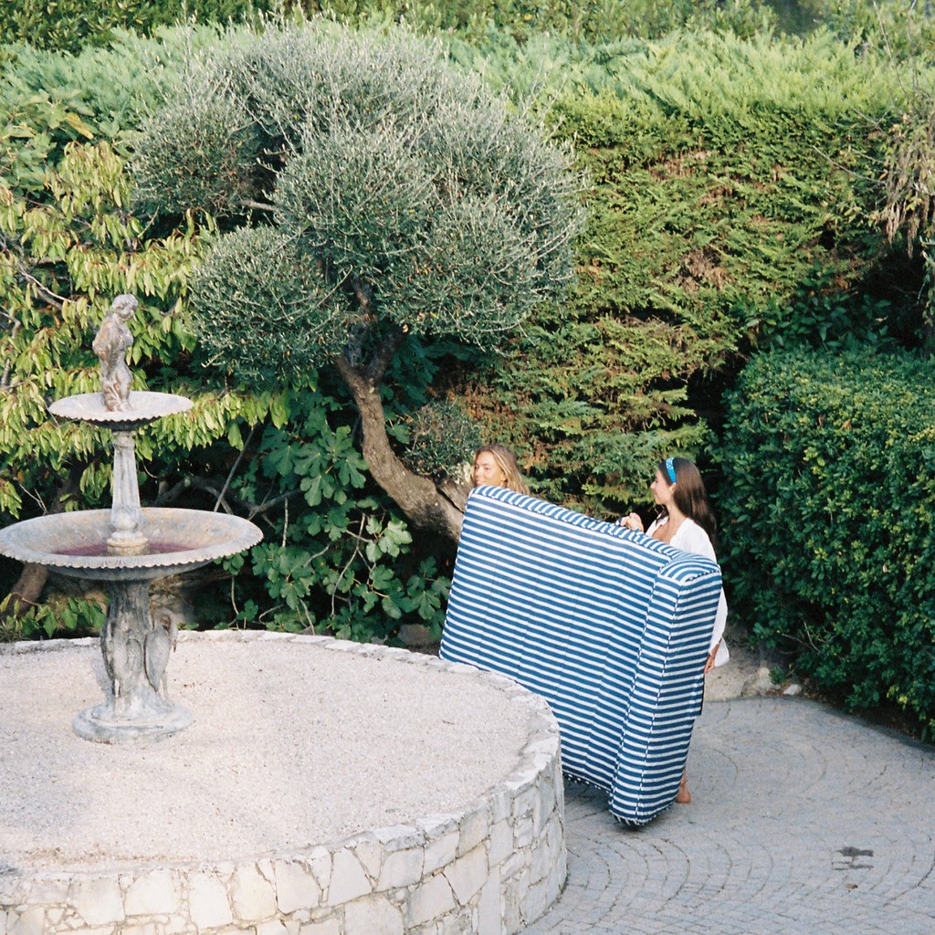 Couple sitting together on a luxury blue-and-white pool float in a Mediterranean garden with stone fountain