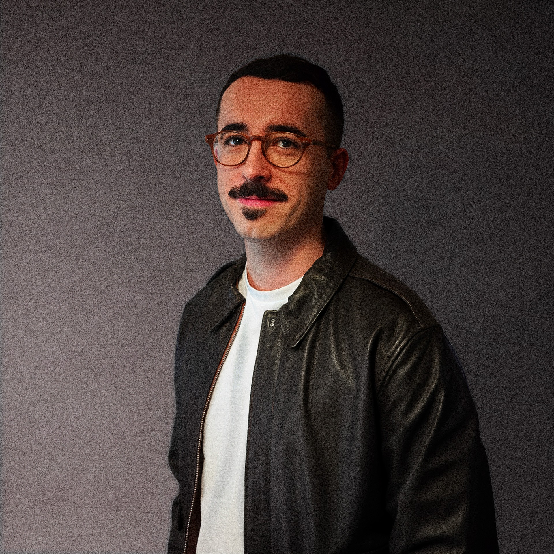 A thoughtful young person with dark hair gazes to the side, captured in soft black and white lighting.